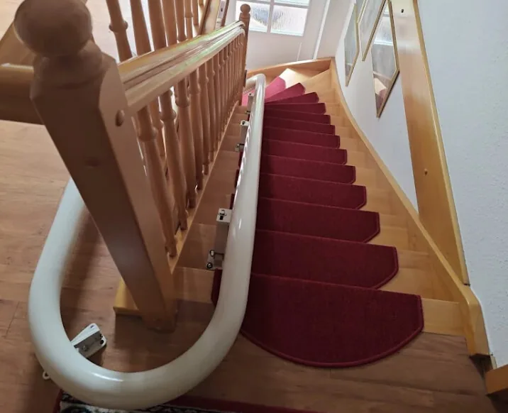 Kurvenschiene entlang einer Holztreppe mit rotem Läufer